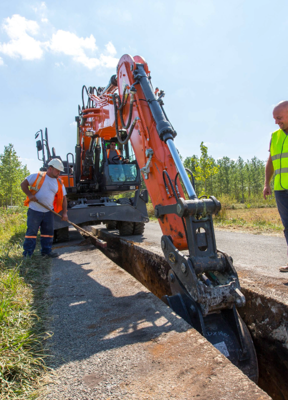 2 personnes devant une tranchée sur la route avec un tractopelle